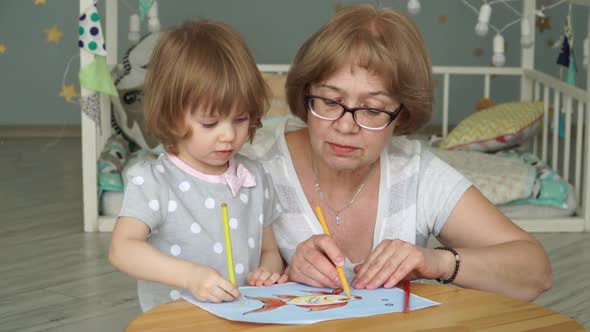Elderly Woman with Girl Paint Goldfish with Pencils