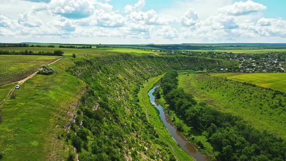 Aerial drone view of a valley in Moldova. River, a lot of greenery, cloudy sky, village alt