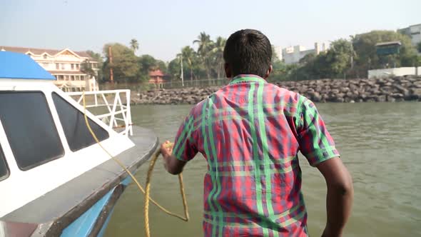 Indian men tying boat to the dock in Mumbai. alt