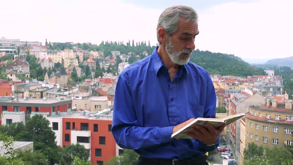 Old Senior Man Man Reads Book - City (Buildings) in Background alt