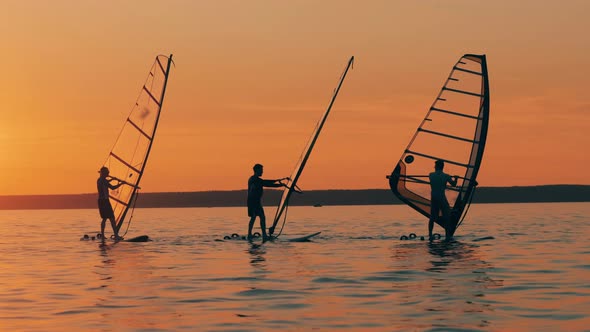 Group of Men Are Windsurfing in the Sea at Sundown alt