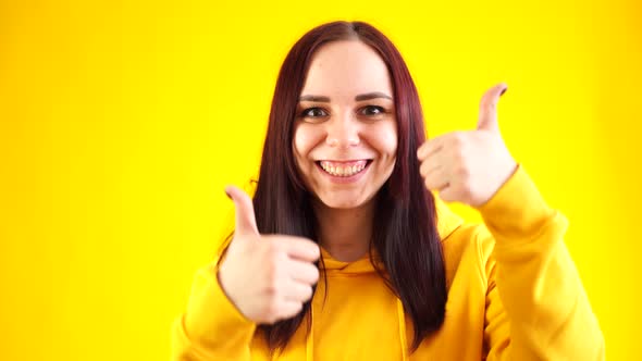 Portrait of Young Woman Smiling and Showing Thumbs Up on Yellow Background alt