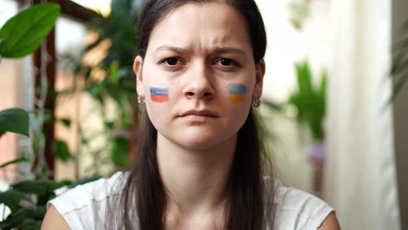 A Young RussianUkrainian Girl with the Flag of Ukraine and Russia on Her Face is Frowning Eyebrows alt