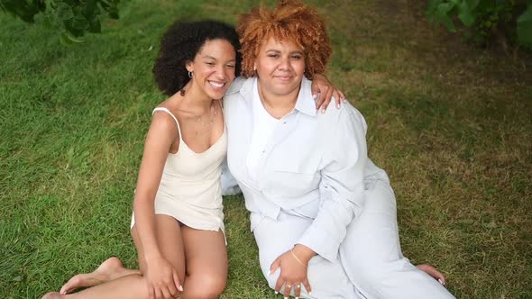 Young Beautiful Happy Lesbian African American Couple Sitting on Green Grass Hugging Outside at