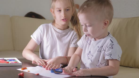 Two Child, Old Sister and Little Brother Playing with Plasticine at Home alt