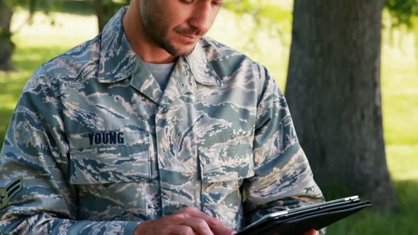Soldier using digital tablet in park alt