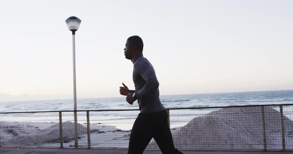 Focused african american man exercising outdoors, running by seaside alt