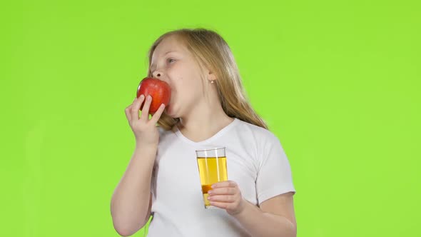Little Girl Drinks Juice From a Glass and Holds an Apple. Green Screen alt