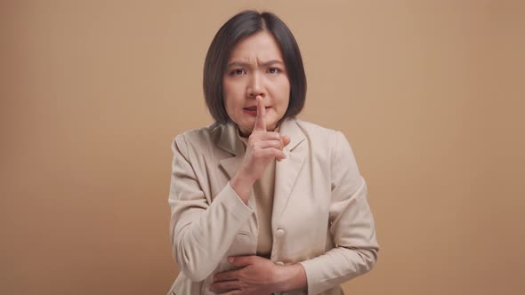 Asian business woman putting index finger on lips meaning keeping secret and standing isolated