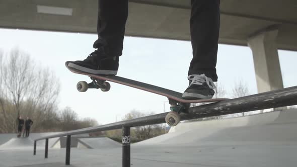 A skater does a backside crooked grind on a flat rail at a concrete skatepark. The shot is in slow-m alt