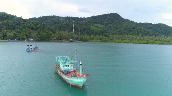 Drone shot of a half sunken boat in the sea being towed by another boat with tropical island in the alt