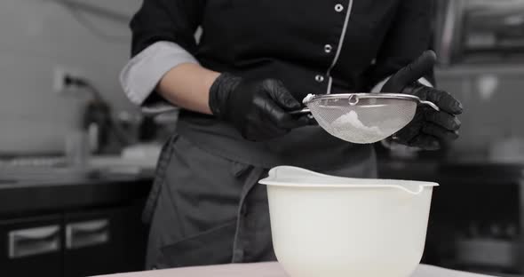 Pastry Chef's Hands in Black Gloves Sifting Flour
