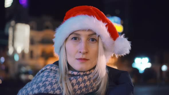 A young woman in a Santa hat looks into the camera . night city. alt