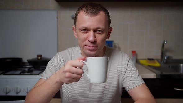 Portrait of a man with a mug of tea at the table in the evening in the kitchen, camera movement alt