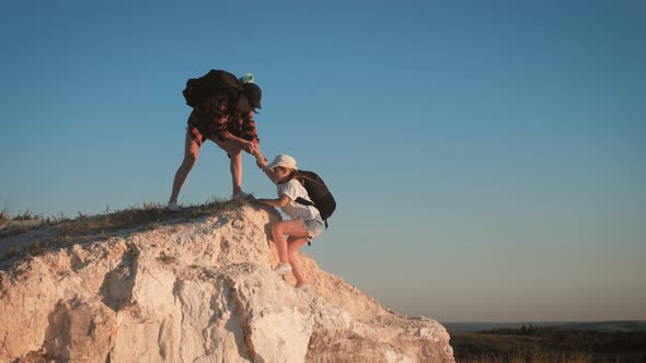 Girl Helps Her Friend Climb Up the Last Section of Mountain. Tourists with Backpacks Help Each Other alt