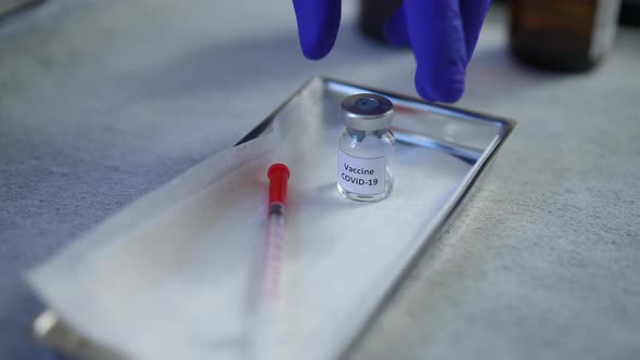Hand in Gloves Taking Coronavirus Vaccine and Syringe From Stainless Steel Medical Tray alt