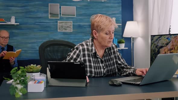 Old Manager Woman Typing on Laptop and Reading on Tablet in Same Time alt