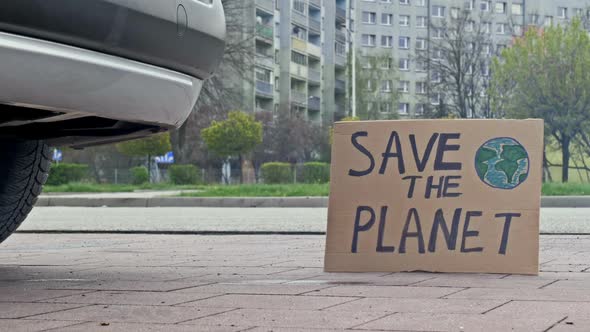 SAVE THE PLANET Poster Next to the Exhaust Pipe of a Car
