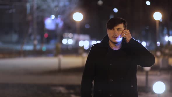 A man is talking on a cell phone on the street at night against the background of night lights.