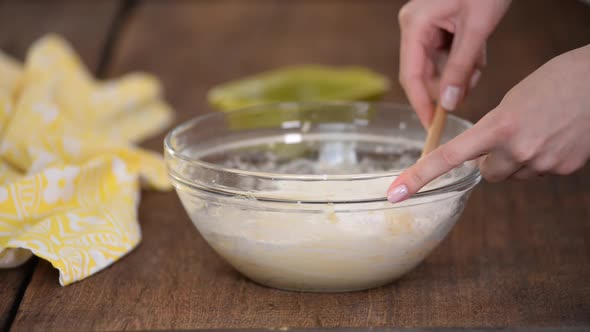 Hands Mixing Batter with a Spatula in a Glass Bowl