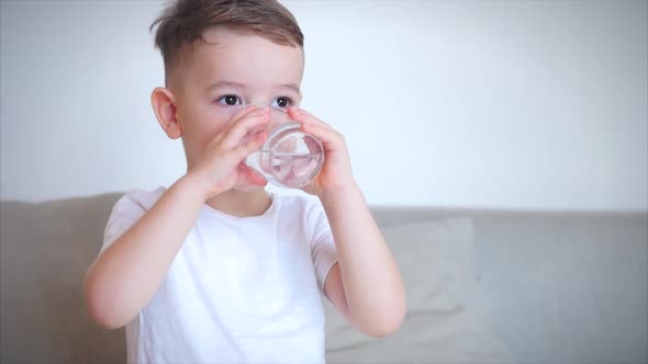 Cute Baby Boy Drinking a Glass of Water Sitting on the Couch at Home. Slow Motion Little Boy alt