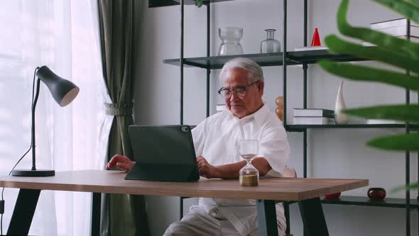 An old Asian man is searching for information on the Internet while sitting at a table. alt