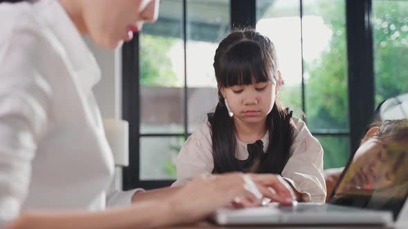 Asian kid feeling sad and need to play with her mom. The mother is busy on working on her job alt