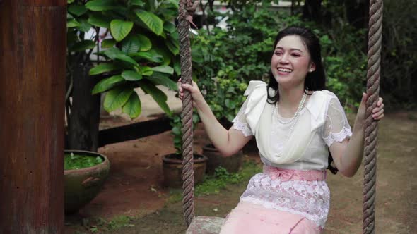 slow-motion of happy young woman in Thai traditional dress relaxing on a wooden swing