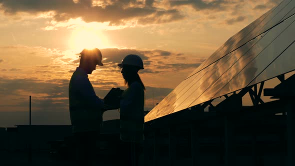 Workers Talk Near Sun Panels on a Sunset Background alt