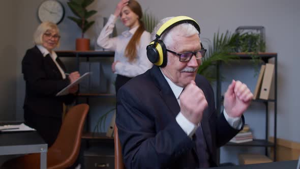 Joyful Senior Businessman Working on Portable Laptop Sitting at Desk Listening Music and Dancing alt