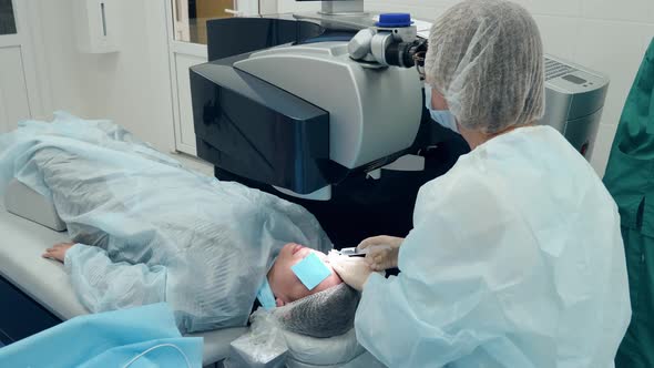 Doctor is Looking Into a Microscope While Operating Patient's Eye alt