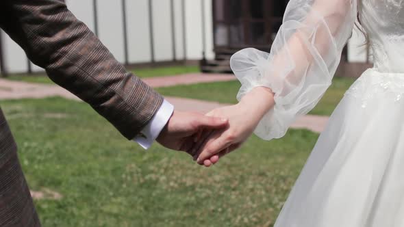 Bride and Groom Holding Hands During Walking in Park at Wedding Day