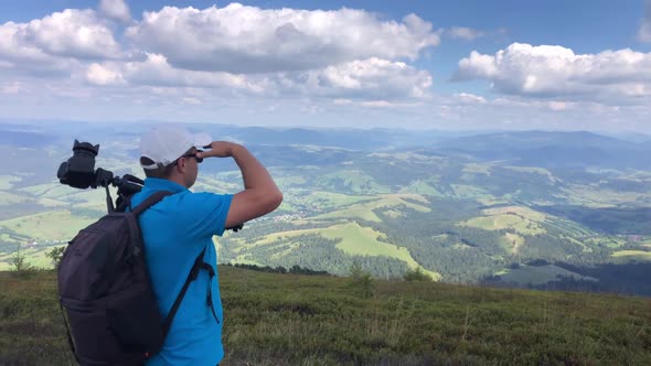A man photographs a mountain landscape while hiking in the mountains. alt