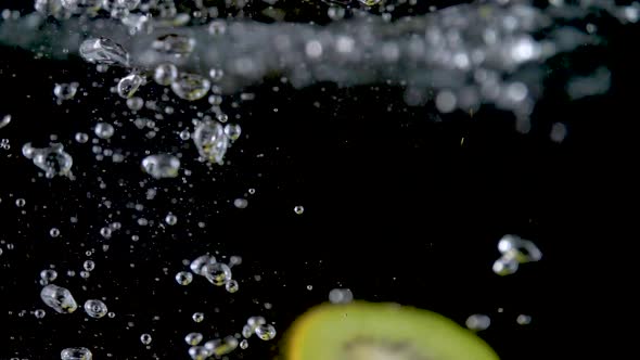 Closeup of fresh kiwis slices falling into clear water with big splash on black background.  alt