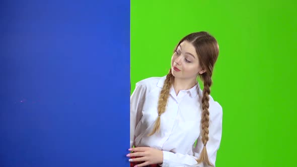 Girl Looks Out From Behind a Blue Board. Green Screen alt