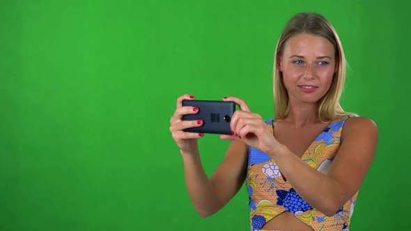 Young Pretty Blond Woman Takes Photos Wirh Smartphone - Green Screen - Studio alt
