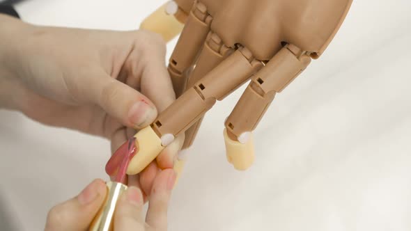 Woman Is Painting Nails Pink Nail Polish on Prosthesis Hand on White Background