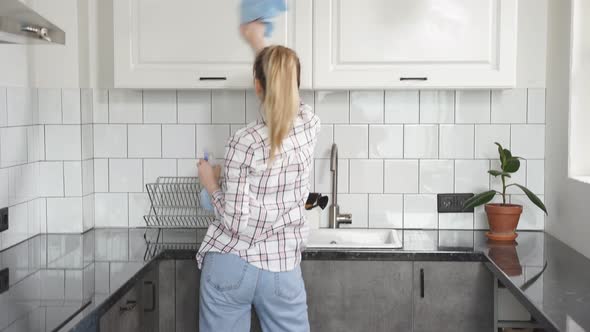 Happy Caucasian Woman Enjoys the Cleaning Process Dancing in Kitchen with Detergents in Her Hands