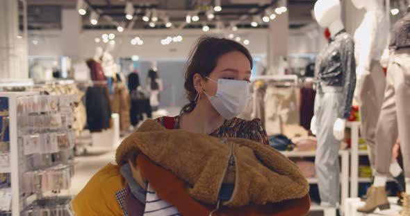 Woman Shopping in Fashion Store Wearing Face Mask Carrying Clothes To Fitting Room alt
