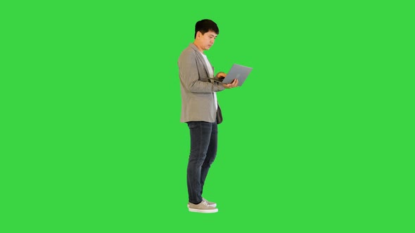 Young Asian Man Types Something Fast on His Laptop and Breathes Out on a Green Screen Chroma Key
