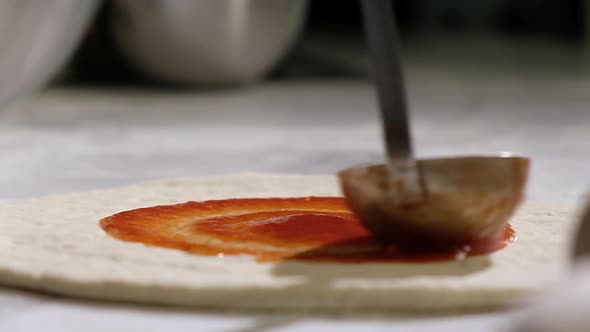 man pours ladle of tomato sauce on dough and spreads. Italian national dish