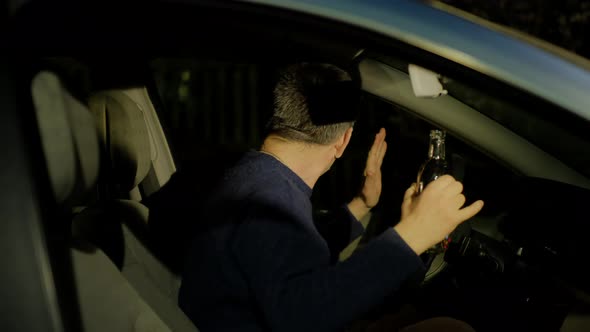 Driver in Sweater Raises Hands with Empty Alcohol Bottle