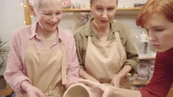 Young Pottery Teacher Checking Clay Bowl of Elderly Female Student alt