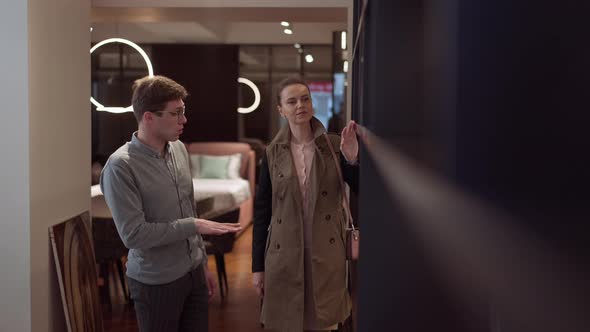 Smiling Woman Choosing Cupboard Listening Man Talking Consulting Client in Furniture Store alt