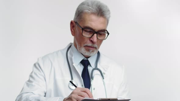 Attending Physician in Glasses and Medical Coat Makes Notes in Tablet Looks Up and Writes Something alt