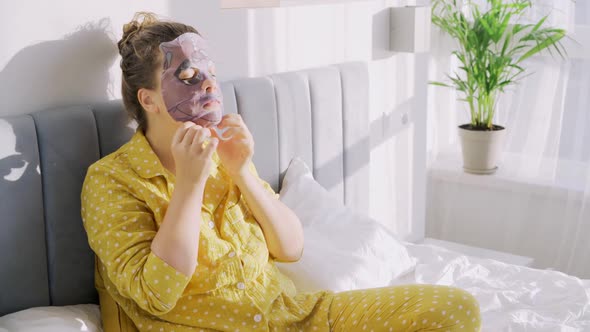 Woman in Pajamas Applying Fascial Mask in Bed