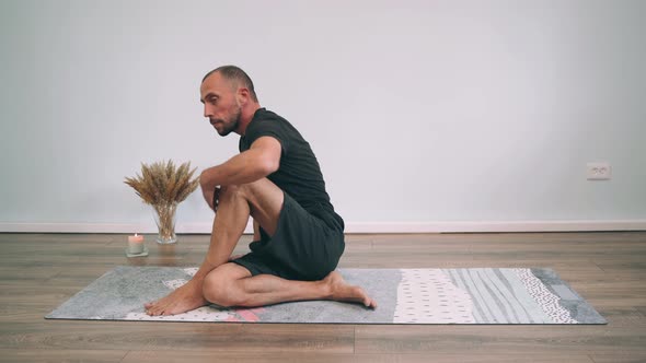 Caucasian Man Does Yoga Online A Man Sits on a Mat and Turns His Legs Half Pose of the King of