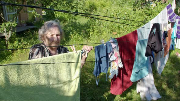 an Elderly Old Woman Hangs Clothes in Her Neglected Garden alt