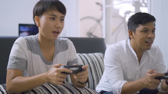 Two friends with joysticks playing video game on couch at home.