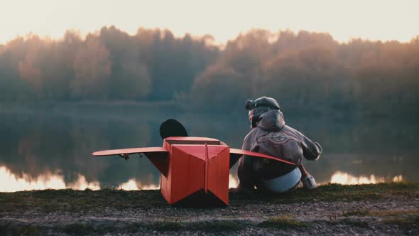 Back View Little Boy in Old Pilot Costume Sitting at Amazing Forest Lake with Fun Red Cardboard alt